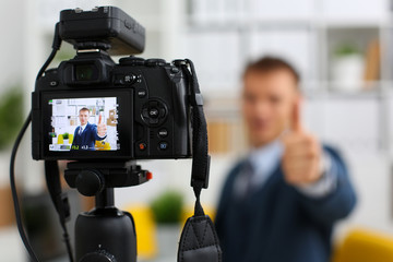 Male in suit and tie show confirm sign arm making promo videoblog or photo session in office camcorder to tripod closeup. Vlogger promotion selfie solution or finance advisor management information