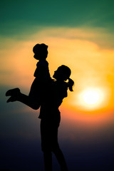 Fototapeta na wymiar silhouette of a family with a happy mother playing with a girl in the sunset sky