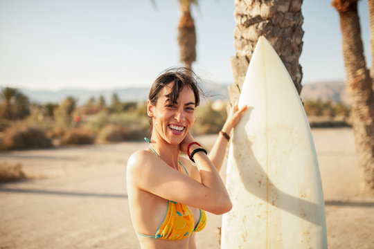 Young smiling woman walking through the beach with her surfboard