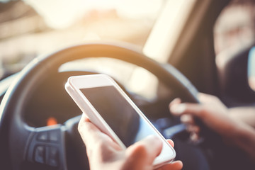 Hand of woman on steering wheel drive a car while using smartphone background.