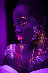 modern fantastic african model posing at camera, fluorescent prints on her body and skin, glowing on ultra violet lights. interesting colorful portrait