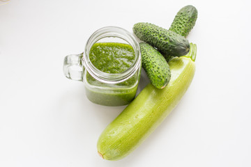 green raw smoothie in a glass cup and green vegetables. Cucumbers and Zucchini