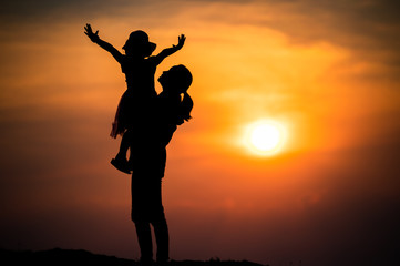 silhouette of a family with a happy mother playing with a girl in the sunset sky