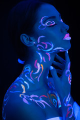 young caucasian fashion model with fluorescent prints on skin, attractive girl posing at camera, bright lines on her skin glows in ultra violet light. isolated black background