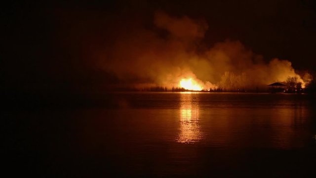 Night forest fire, reflected on the water surface of the river