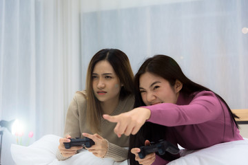 Young beautiful Asian woman lgbt couple playing console game together fight for winner with joy and serious mood on bed in bedroom at night time