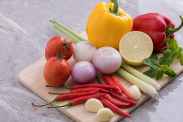 Herbs used for making soup and salad are tomatoes, lemongrass, onions, garlic, chili, lemon and mint leaves. All placed on a wooden cutting board.