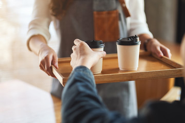 A waitress holding and serving paper cups of hot coffee to customer in cafe