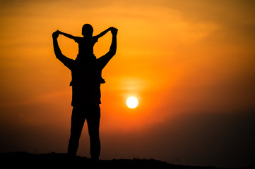 silhouette of a family with a boy riding his father's neck happily against the sunset sky