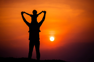 Fototapeta premium silhouette of a family with a boy riding his father's neck happily against the sunset sky