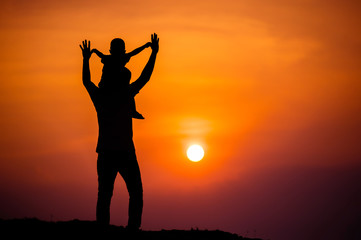 Fototapeta premium silhouette of a family with a boy riding his father's neck happily against the sunset sky