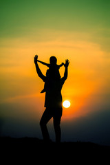 silhouette of a family with a boy riding his father's neck happily against the sunset sky