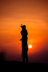 silhouette of a family with a boy riding his father's neck happily against the sunset sky