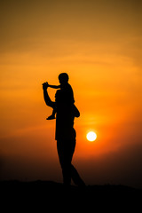 silhouette of a family with a boy riding his father's neck happily against the sunset sky