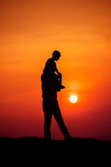 silhouette of a family with a boy riding his father's neck happily against the sunset sky