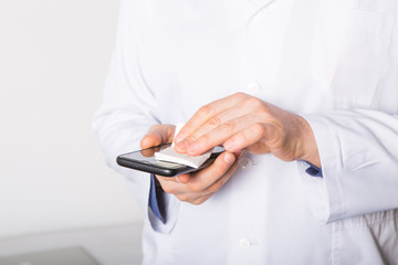  Doctor disinfecting cleaning mobile phone screen preventive wiping for SARS-CoV-2 . COVID-19 Pandemic Coronavirus.