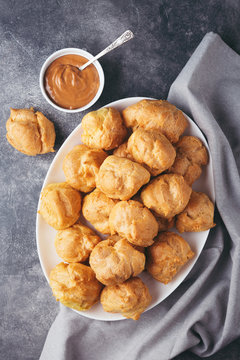Top view on profitroles on white plate and caramel on stone table with napkin. Traditional french dessert.