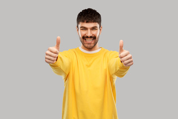 gesture and people concept - smiling young man in yellow sweatshirt showing thumbs up over grey background