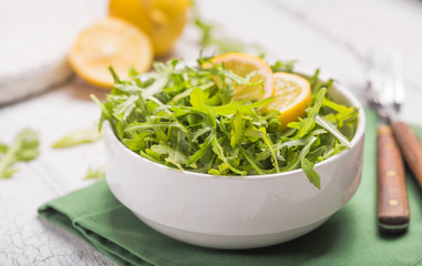 Fresh green arugula leaves on white bowl, rucola rocket salad on wooden rustic background with place for text. Selective focus,  healthy food, diet. Nutrition concept
