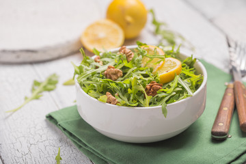 Fresh green arugula leaves on white bowl, rucola rocket salad on wooden rustic background with place for text. Selective focus,  healthy food, diet. Nutrition concept