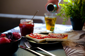 Sweet breakfast with freshly made jam on toast and a very hot tea or honey camomile served by a girl. She also spreads the jam