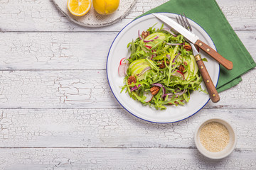 Fresh green arugula leaves on white bowl, rucola rocket salad with apple, radish, pecan nuts, onion on wooden rustic background with place for text. Top view,  healthy food, diet. Nutrition concept