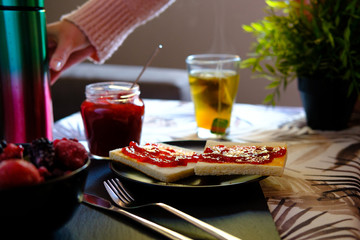 Sweet breakfast with freshly made jam on toast and a very hot tea or honey camomile served by a girl. She also spreads the jam