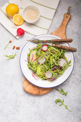 Fresh green arugula leaves on white bowl, rucola rocket salad with apple, radish, pecan nuts, onion on wooden rustic background with place for text. Top view,  healthy food, diet. Nutrition concept
