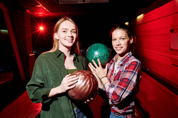 Two pretty cheerful female players with bowling balls looking at you before game