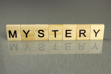 the word mystery is made up of square wooden letters on a gray background. Concept for mysteries,...