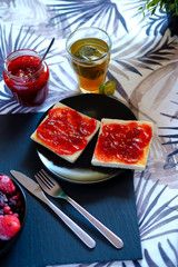 Sweet breakfast with freshly made jam on toast and a very hot tea or honey camomile served by a girl. She also spreads the jam