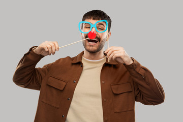 party props, photo booth and people concept - happy smiling young man with paper glasses and red clown nose over grey background
