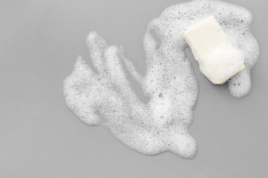 Soap bar with bubbles on grey background top-down