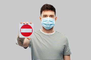 health protection, safety and pandemic concept - young man in protective medical mask showing stop sign over grey background