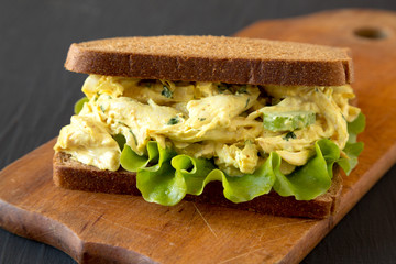 Homemade Coronation Chicken Sandwich on a rustic wooden board on a black surface, low angle view. Close-up.