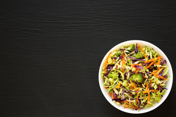 Homemade Raw Shredded Broccoli Slaw in a white bowl on a black background, top view. Flat lay, overhead, from above. Copy space.