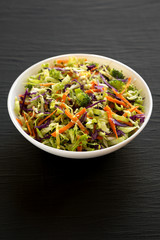 Homemade Raw Shredded Broccoli Slaw in a white bowl on a black surface, side view.