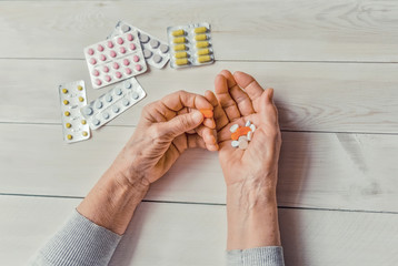 Obraz premium Senior hands with pills and drugs on light table, wooden background. Wrinkled hands of old woman holding colorful tablets. Painful old age. Health care for the elderly.