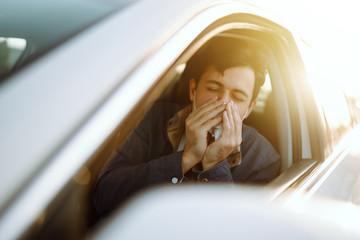 Young man coughing and sneezing into a handkerchief while driving a car. The concept of preventing the spread of the epidemic and treating coronavirus, pandemic in quarantine city. Covid -19.