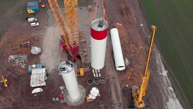 Building process of wind energy power tower mill, under construction. Installation tower, workers inside assembling the pillar of windmill. Green, clean, renewable energy. Aerial footage.