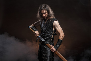 Man dressed in medieval armour and raincoat with longs word over smoke background. Courage fantasy...