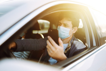 Young man in protective sterile medical mask on her face using phone in the car. The concept of preventing the spread of the epidemic and treating coronavirus, pandemic in quarantine city.