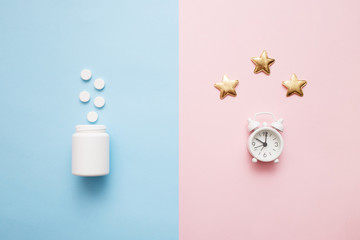 Pills, bottle and white alarm clock with stars on pink, blue art background. Concept Insomnia, sleep problems, time to take pills and treatment. Top view, flat lay, copy space