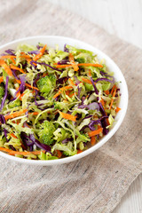 Homemade Raw Shredded Broccoli Slaw in a white bowl on cloth, side view. Close-up.