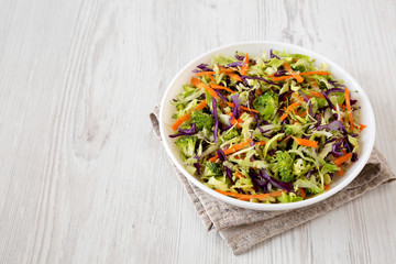 Homemade Raw Shredded Broccoli Slaw in a white bowl on cloth, side view. Copy space.