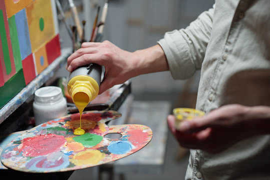 Hand of young painter adding yellow color on palette before start painting