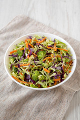 Homemade Raw Shredded Broccoli Slaw in a white bowl on cloth, low angle view. Close-up.