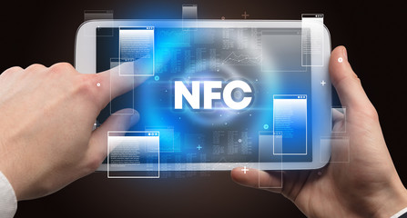 Close-up of a hand holding tablet with NFC abbreviation, modern technology concept