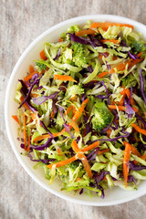 Homemade Raw Shredded Broccoli Slaw in a white bowl on cloth, view from above. Top view, overhead, flat lay.