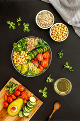 Veggie bowl. Vegetable salad with quinoa, avocado, tomato, spinach and chickpeas - on black table. Top view